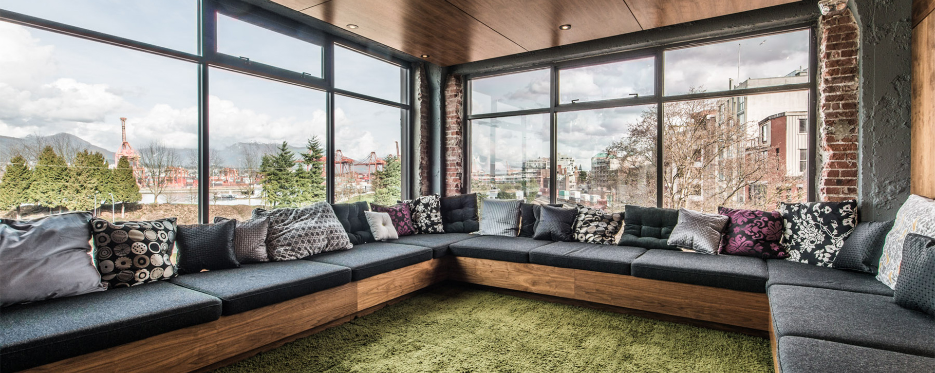 An indoor sitting area at Industrial Light & Magic's Vancouver studio. There is a large sectional full of pillows surrounded by large windows with views of the city.