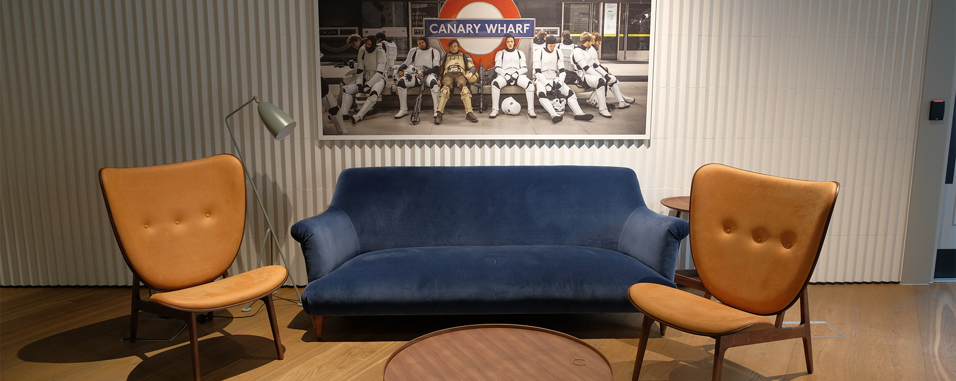 The lobby of Industrial Light & Magic's London Studio. There is a velvet navy blue sofa with tan leather chairs on each side, and a large piece of art above it.