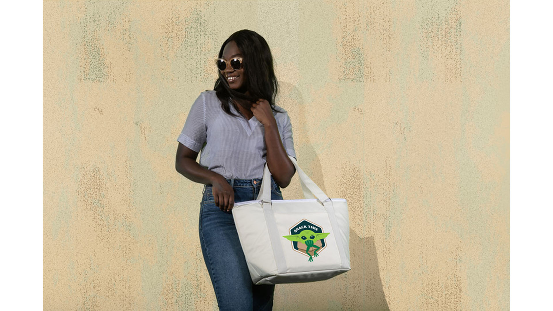 A young woman holding a white cooler tote featuring The Child from Star Wars: The Mandalorian eating a frog.