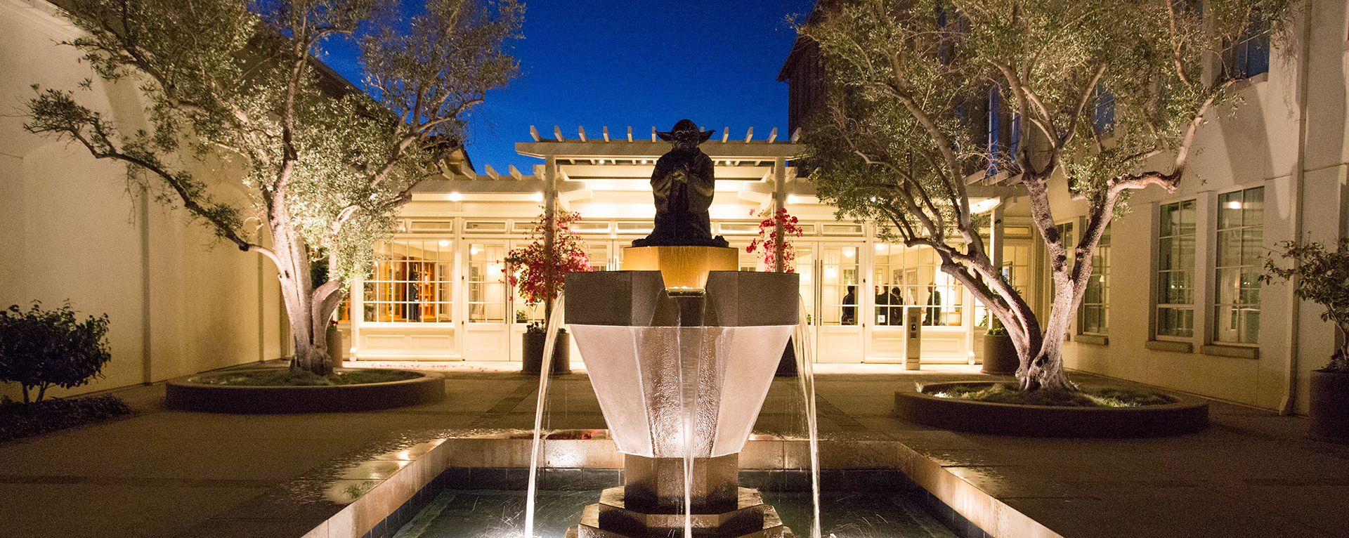 The Yoda fountain is lit up at night, with the entrance to Building B of the Letterman Digital Arts Center in the Presidio of San Francisco, California in the background.