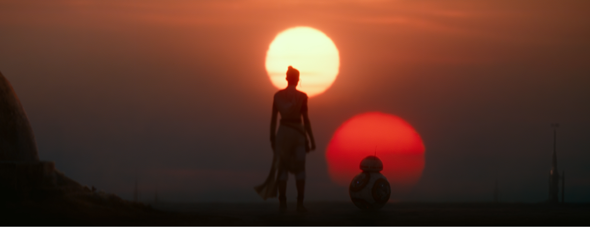 A film still from Star Wars: Rise of Skywalker. Rey and BB-8 look at the setting twin suns on Tatooine.